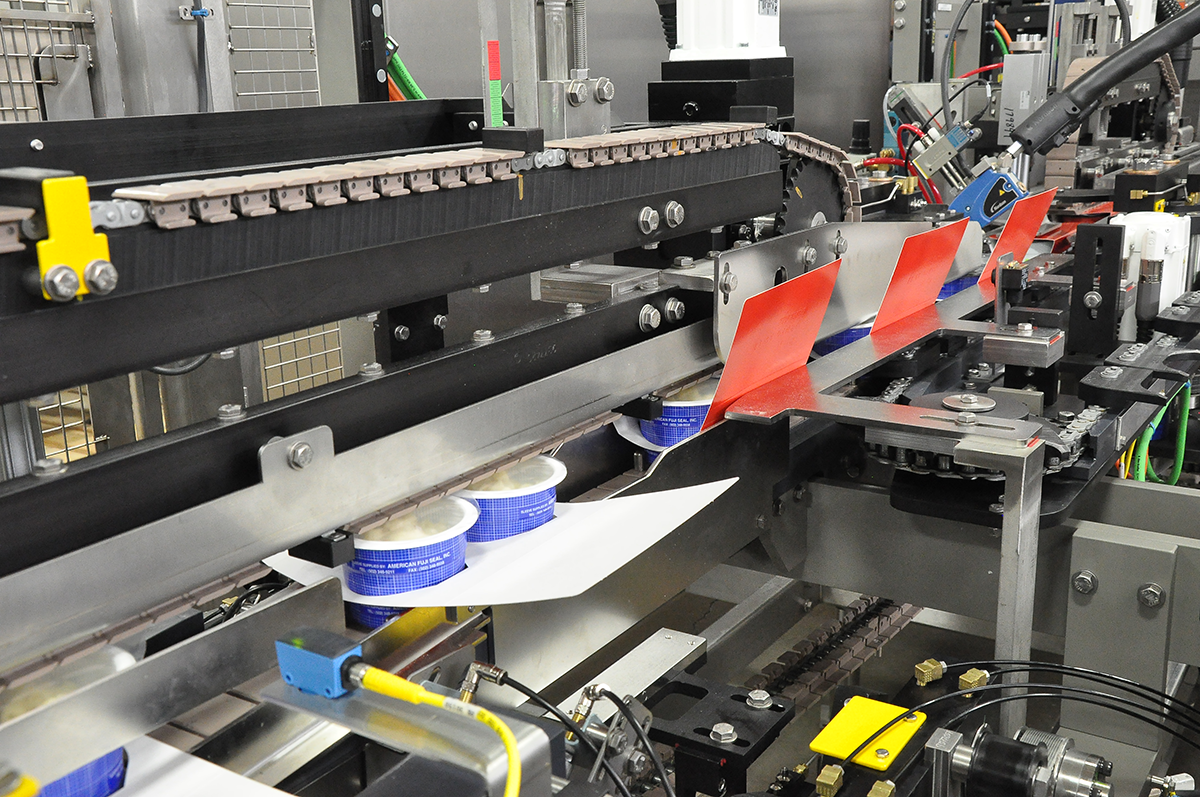 Overwrapper equipment packaging food cups in a drop-through paperboard sleeve