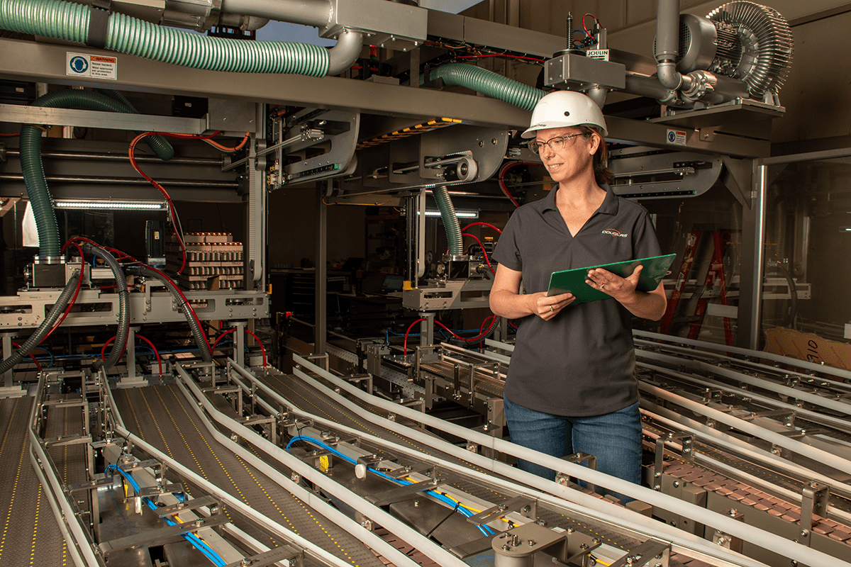 Worker wearing hardhat and holding clipboard observing machine conveyor lines