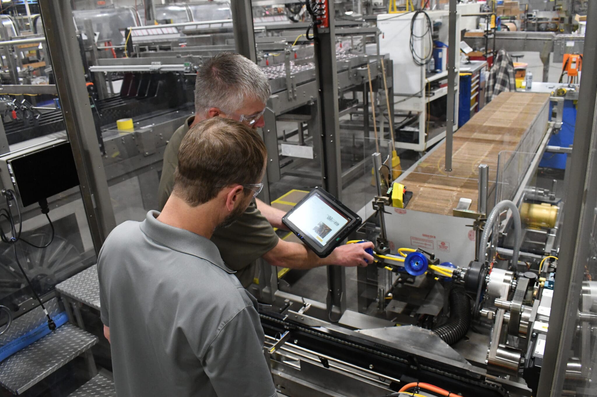 Men Working on Tablet by Packaging Machine